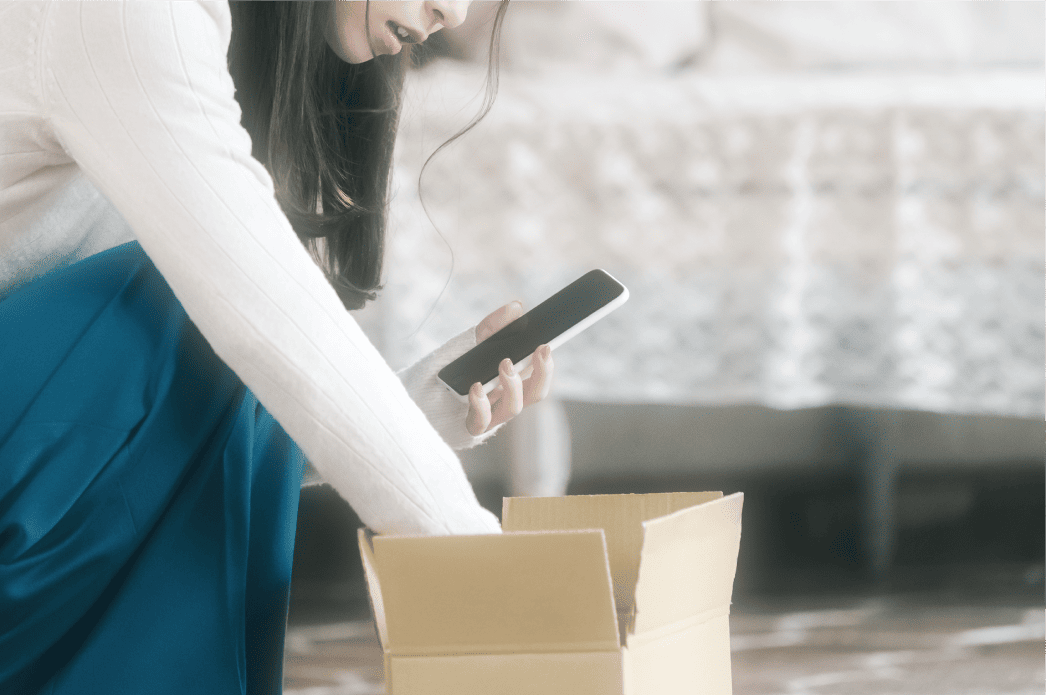 届いた荷物の箱を開けながらスマホを見る女性